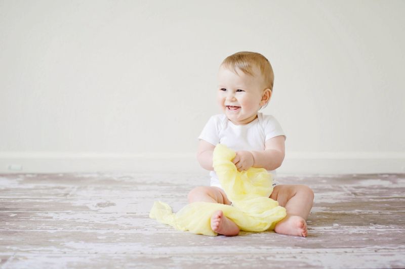Siedzące i śmiejące się niemowle, które bawi się tkaniną koloru żółtego.