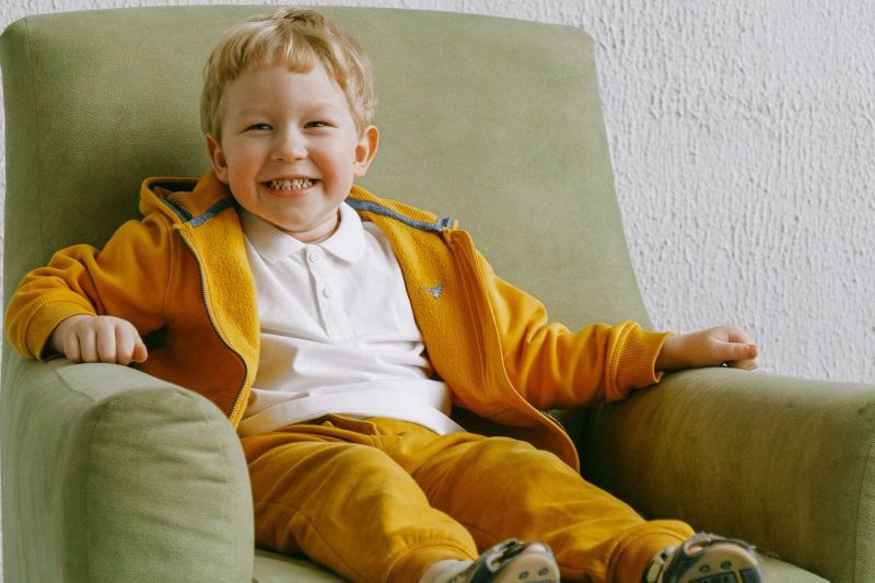 Uśmiechnięty chłopiec w żółtym ubranku na zielonym fotelu.